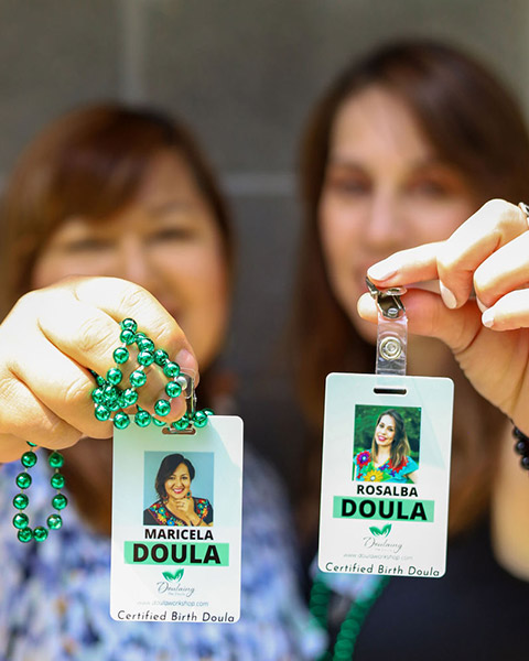 Two doula's holding their certified doula badges