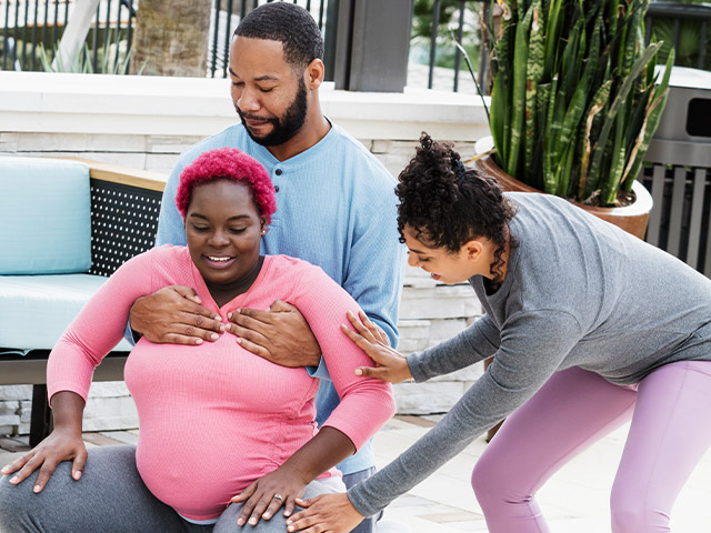 A doula is helping birthing parents with exercise technique on the birthing ball