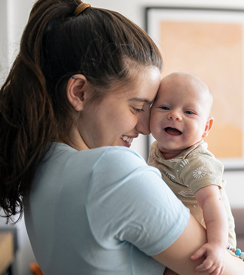Postpartum birthing parent smiling and hugging newborn baby